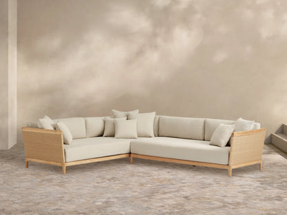 Puglia Outdoor Teak L-shaped Sectional with natural teak frame, light cream cushions, and woven wicker accents on an outdoor patio.