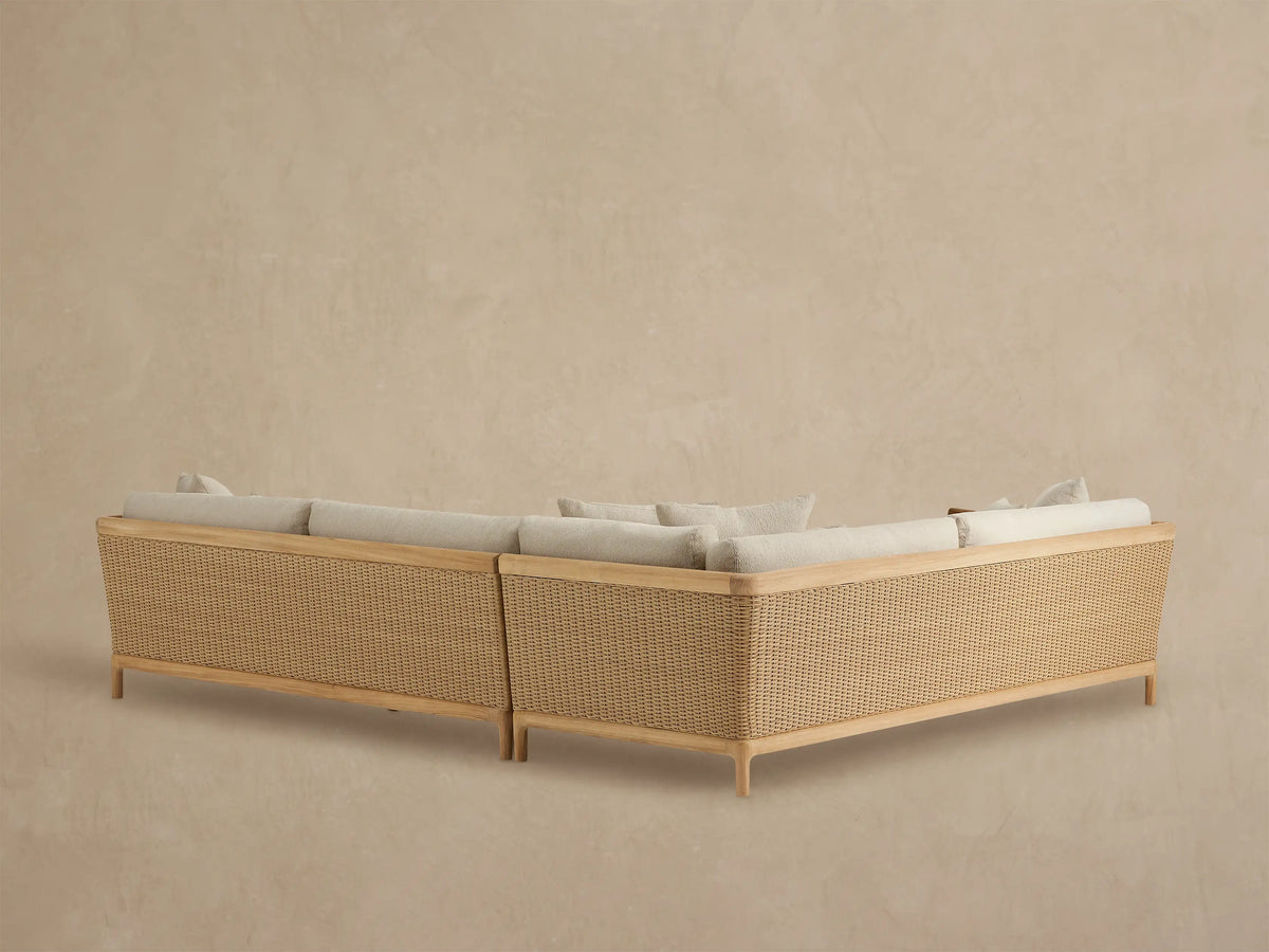 Puglia outdoor sectional close-up: light beige ribbed cushions, natural teak armrest, woven tan resin wicker side panel.