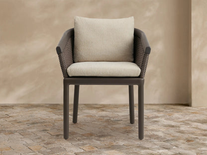 Puglia Outdoor Aluminum Dining Chair with dark brown frame & woven back, light cream seat & back cushions, on stone.