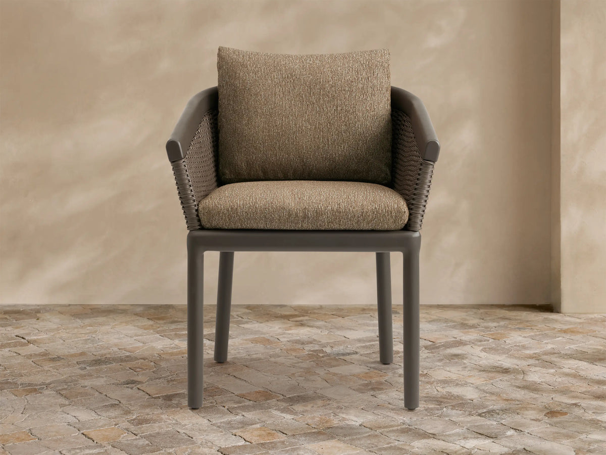 Puglia Outdoor Aluminum Dining Chair. Dark gray frame, brown woven wicker back/arms, and textured tan cushions on a patio.