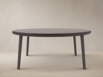 Puglia Outdoor Aluminum Round Dining Table in dark gray, with a slatted top and four sturdy legs, on a patterned stone patio.