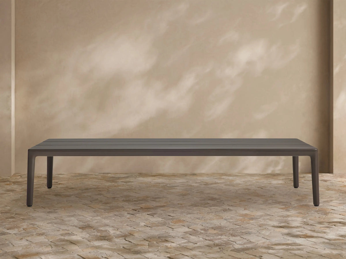 Rectangular dark grey Puglia Outdoor Aluminum Coffee Table with a slatted top, shown outdoors on a light brown textured patio.