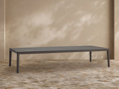 Rectangular dark grey Puglia Outdoor Aluminum Coffee Table with a slatted top, shown outdoors on a light brown textured patio.
