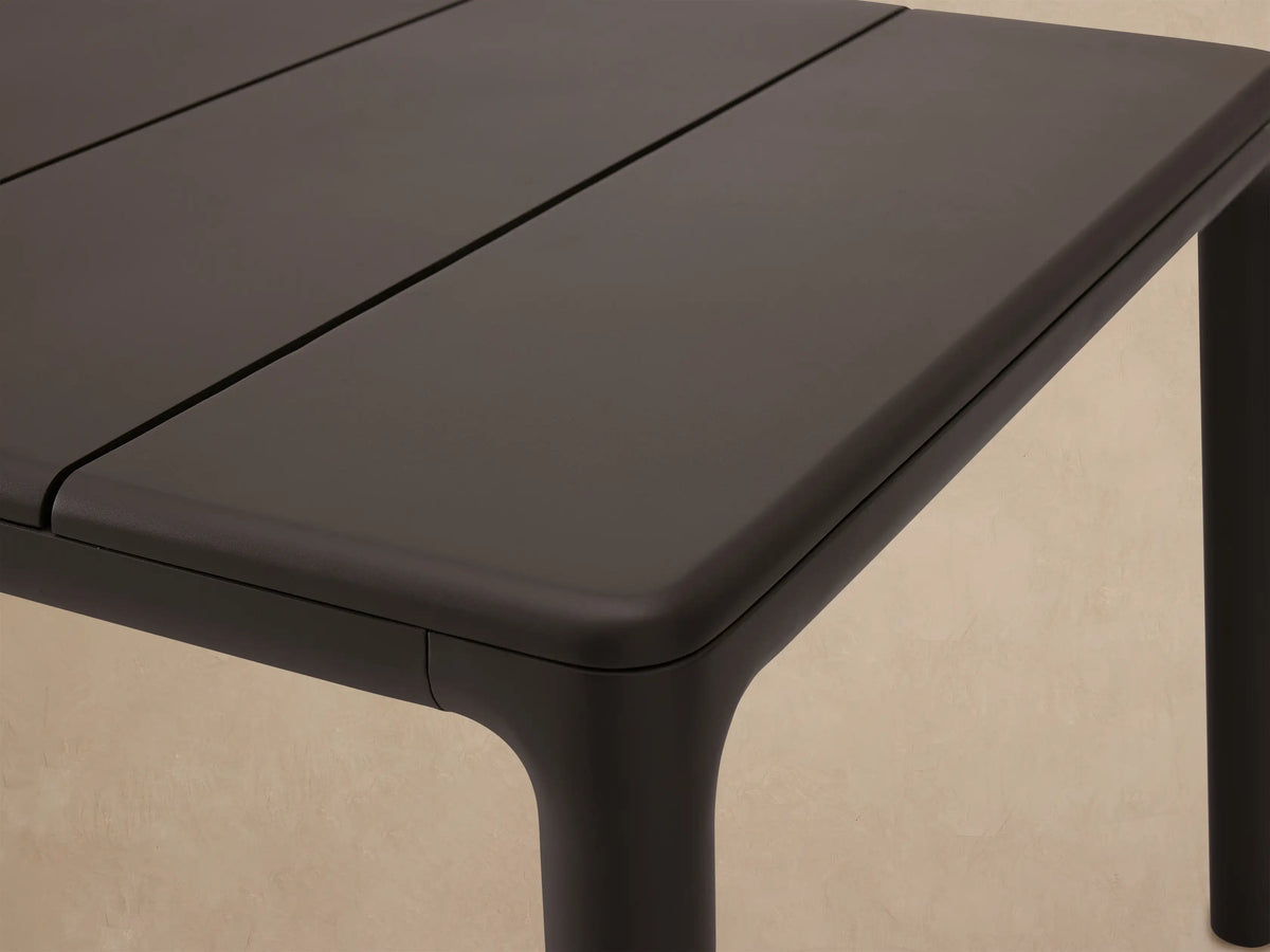 Rectangular Puglia Outdoor Aluminum Dining Table in dark gray, with a slatted top and straight legs, on a tiled patio.