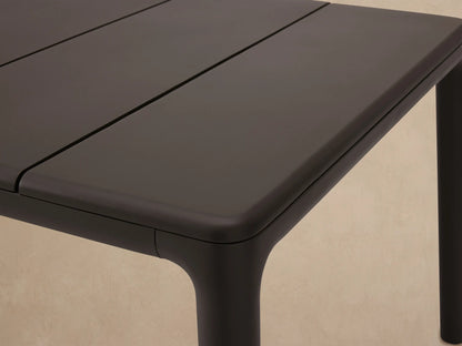 Rectangular Puglia Outdoor Aluminum Dining Table in dark gray, with a slatted top and straight legs, on a tiled patio.