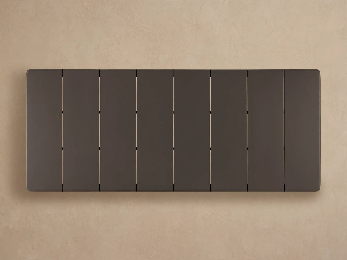 Close-up, angled view of a dark gray Puglia Outdoor Aluminum Dining Table's rounded corner, with tabletop panel lines and sturdy leg.