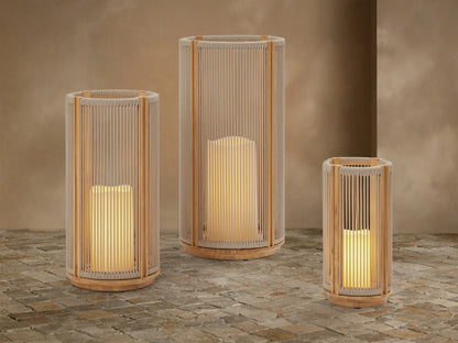 Three Ravello Outdoor Lanterns of varying sizes with natural teak frames and woven beige rope, each glowing with a flameless candle, on a stone patio.