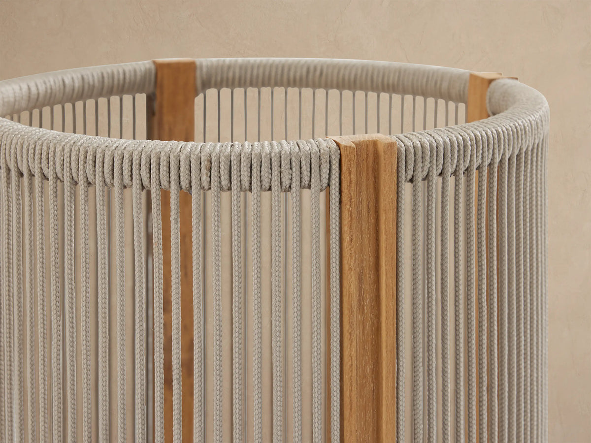 Three Ravello Outdoor Lanterns of varying sizes with natural teak frames and woven beige rope, each glowing with a flameless candle, on a stone patio.