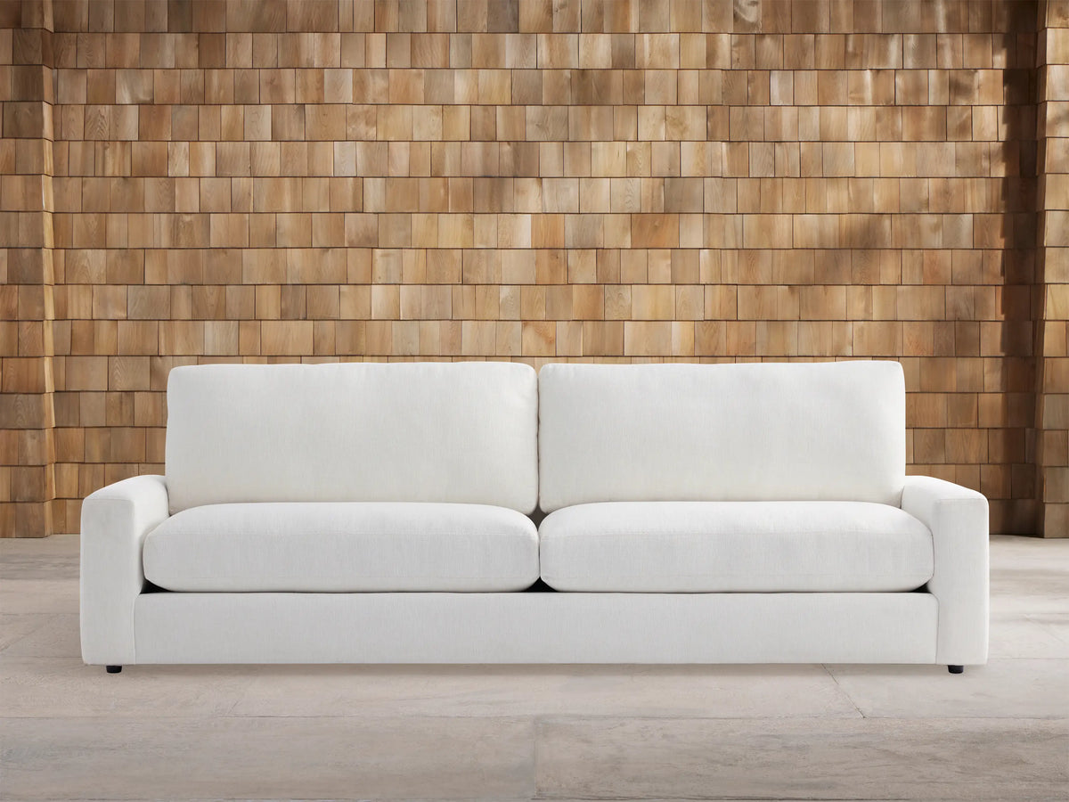 Remington Outdoor Sofa, Eden Snow white, with two seat & back cushions, shown front-facing against a wood shingle wall.
