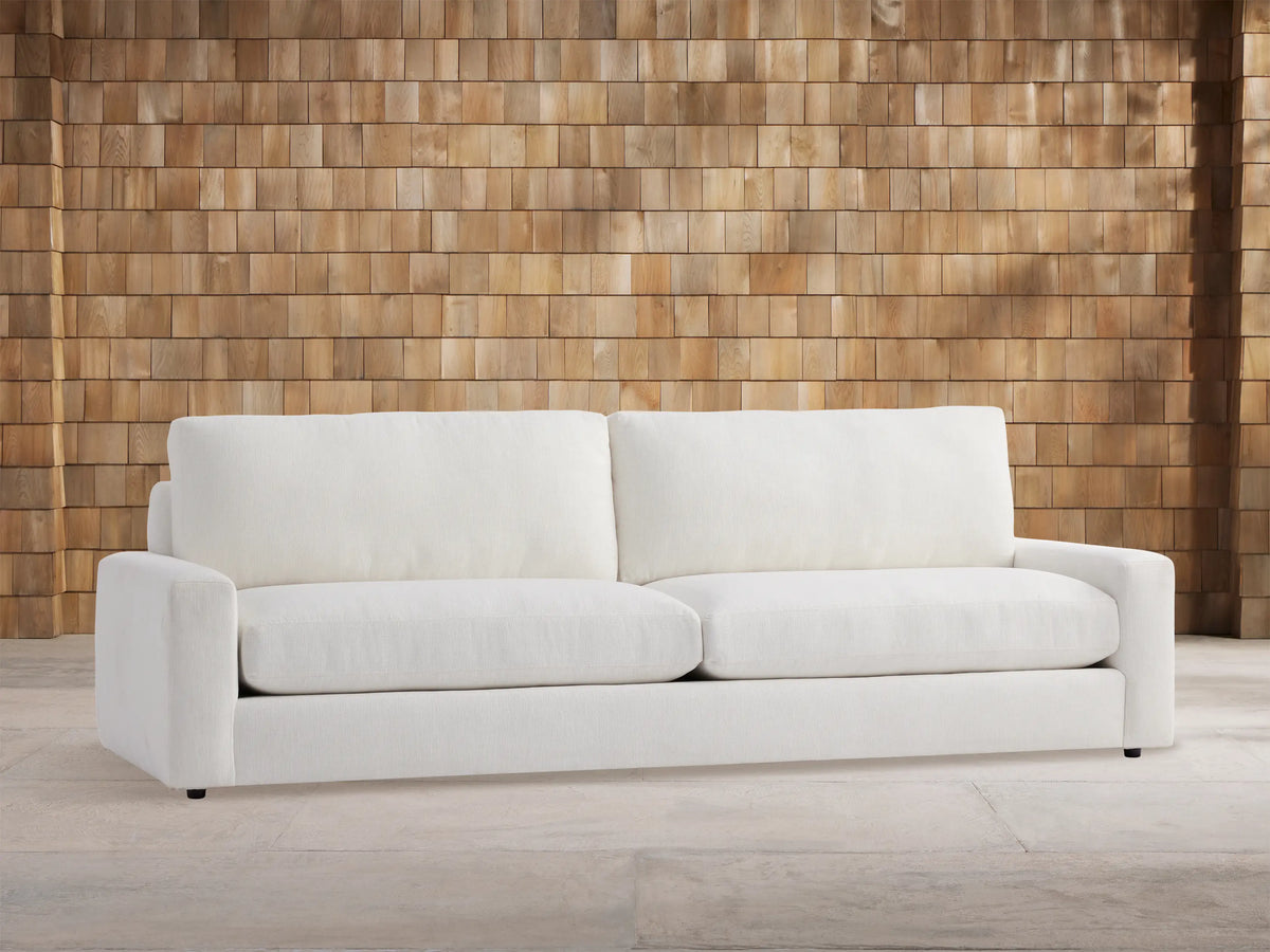 Remington Outdoor Sofa, Eden Snow white, with two seat & back cushions, shown front-facing against a wood shingle wall.