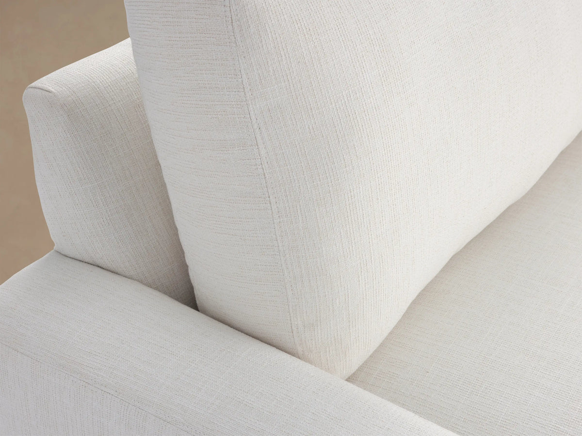Remington Outdoor Sofa in Eden Snow: a modern white sofa with two plump cushions & wide arms, against a wooden shingle wall.