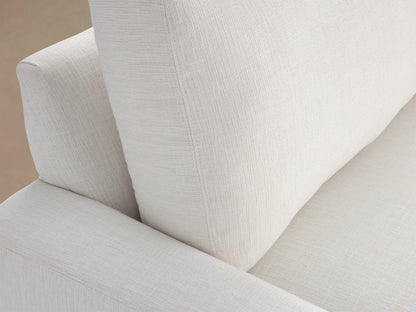 Remington Outdoor Sofa in Eden Snow: a modern white sofa with two plump cushions & wide arms, against a wooden shingle wall.