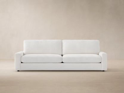Remington Outdoor Sofa, Eden Snow white, with two seat & back cushions, shown front-facing against a wood shingle wall.