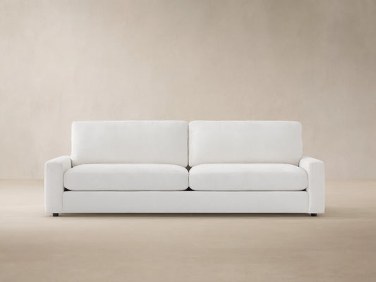 Remington Outdoor Sofa, Eden Snow white, with two seat & back cushions, shown front-facing against a wood shingle wall.