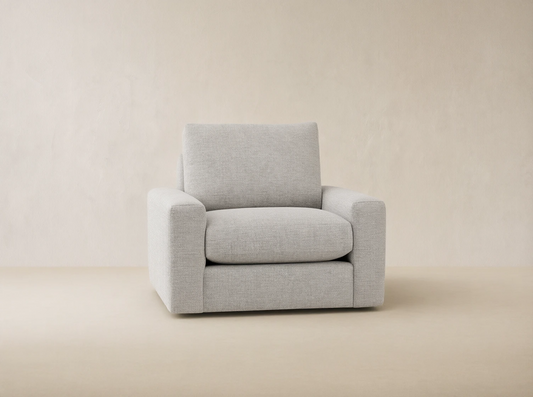Light grey Remington Outdoor Swivel Chair with plush cushions, featuring square arms, set against a wooden shingle wall background.