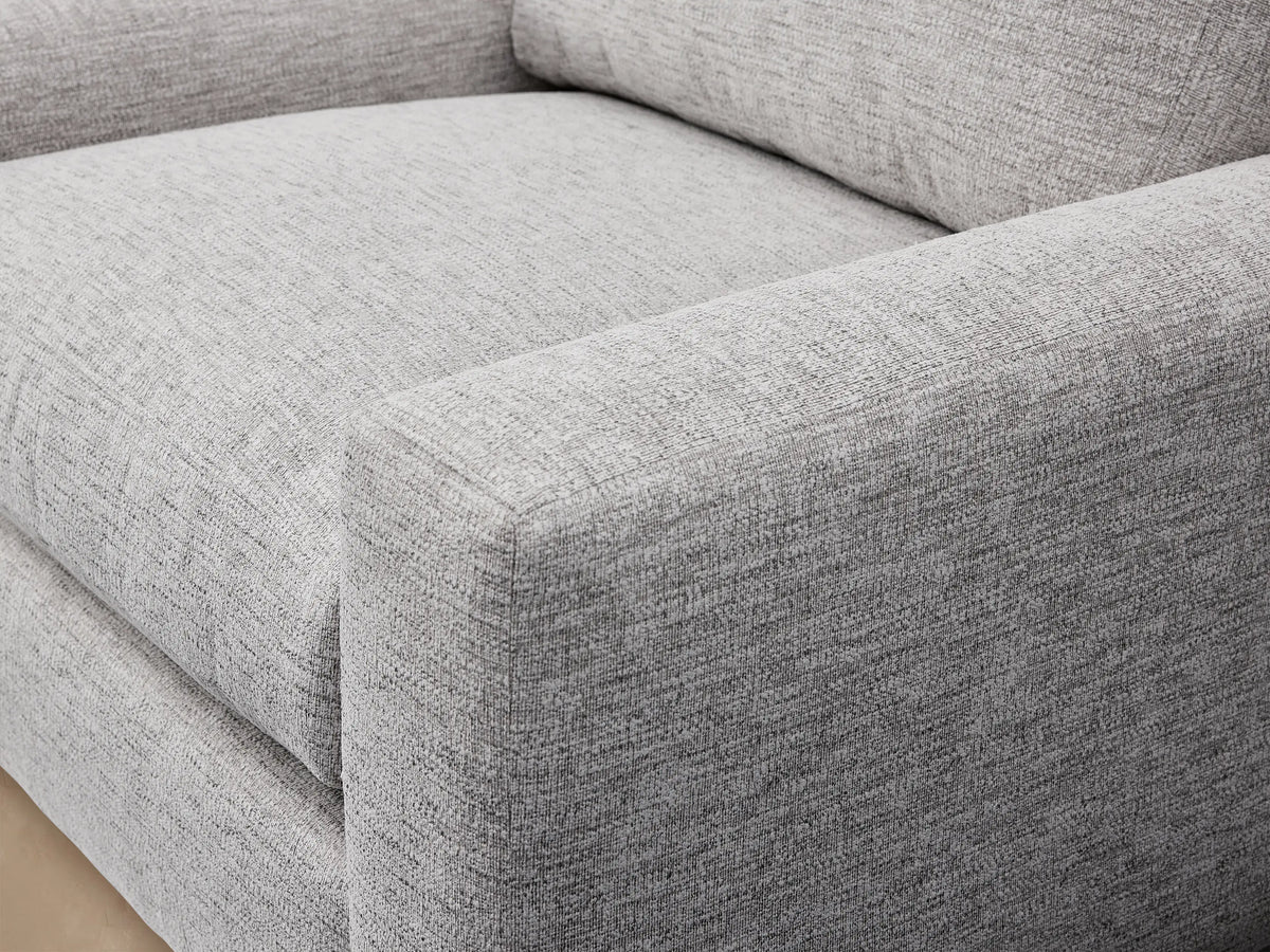 Light grey Remington Outdoor Swivel Chair with plump cushions and square arms, against a textured wooden shingle wall and light floor.
