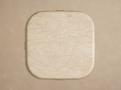 Reily Outdoor End Table. Close-up of its cream marble top with brown veining and rounded edge resting on a light teak wood base.