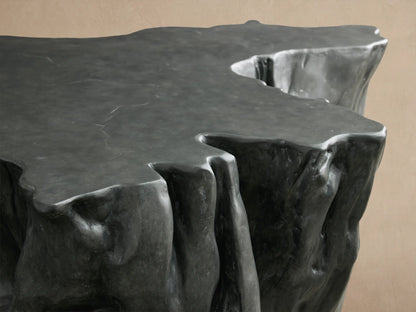 Dark charcoal Root Outdoor Coffee Table, sculpted like a tree root from concrete, featuring a smooth top and rugged, textured sides.