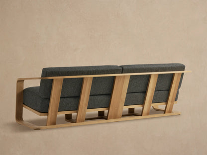 Sonoma Outdoor Teak Sofa close-up: smooth light teak armrest, dark grey marled fabric cushions, angled against beige.