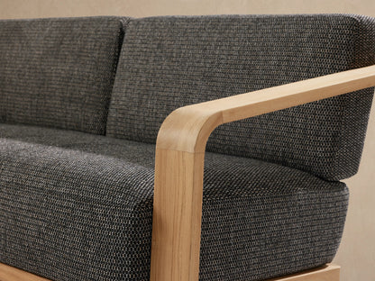 Sonoma Outdoor Teak Sofa, light natural teak frame with curved arms, dark gray textured cushions, presented slightly angled.