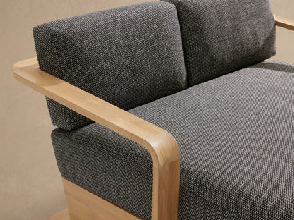 Sonoma Outdoor Teak Daybed with a light natural teak frame and dark grey textured cushions, seen from the side against a neutral wall.