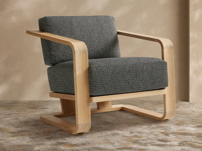 Sonoma Outdoor Teak Lounge Chair with light wood frame and dark gray, textured cushions, viewed from front-left on a tiled floor.