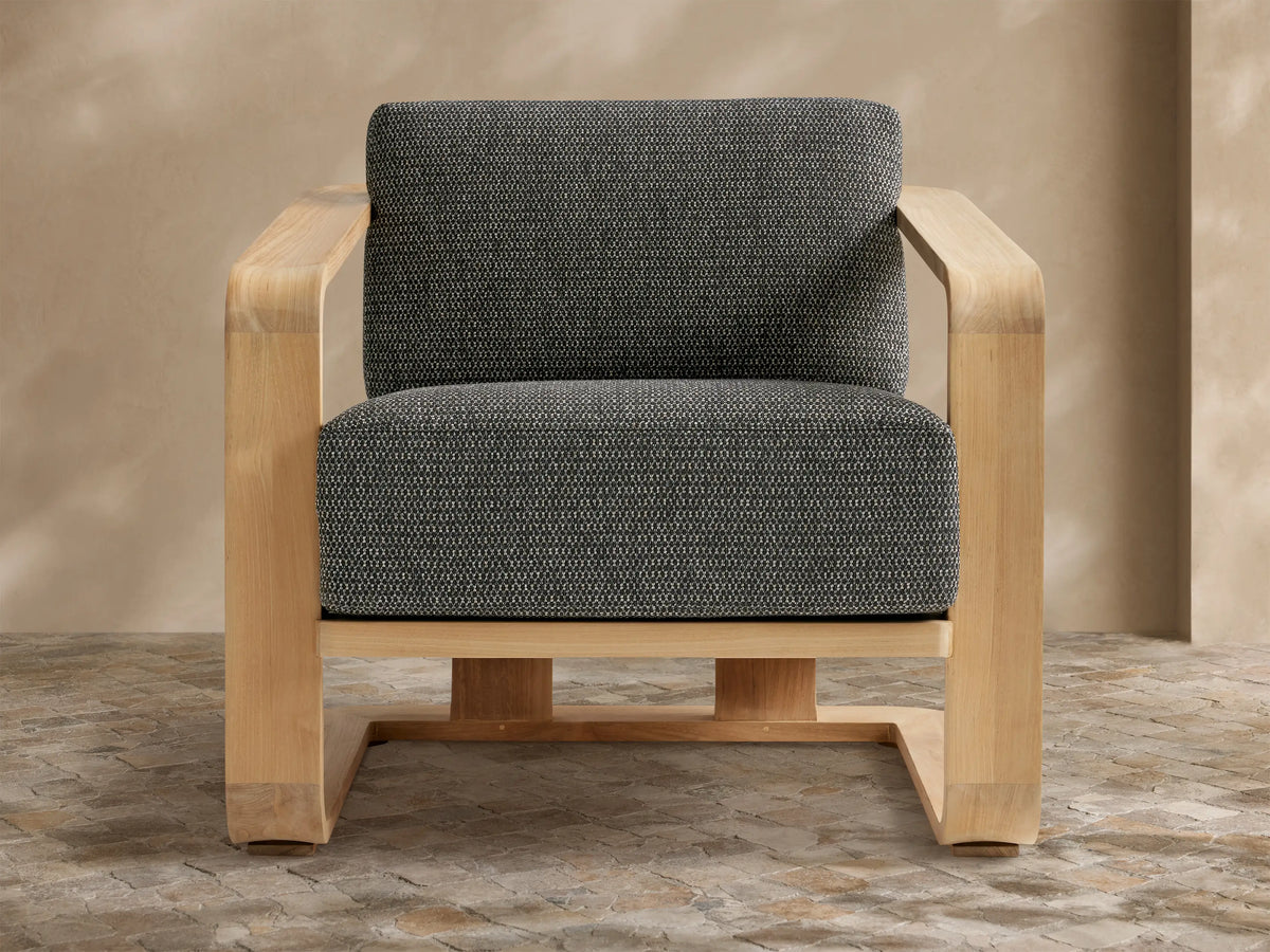 Sonoma Outdoor Teak Lounge Chair with light wood frame and dark gray, textured cushions, viewed from front-left on a tiled floor.