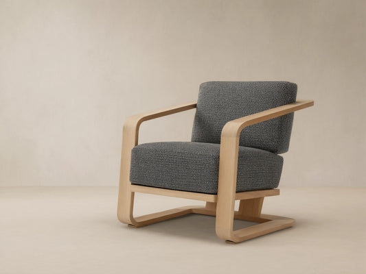 Sonoma Outdoor Teak Lounge Chair with light wood frame and dark gray, textured cushions, viewed from front-left on a tiled floor.