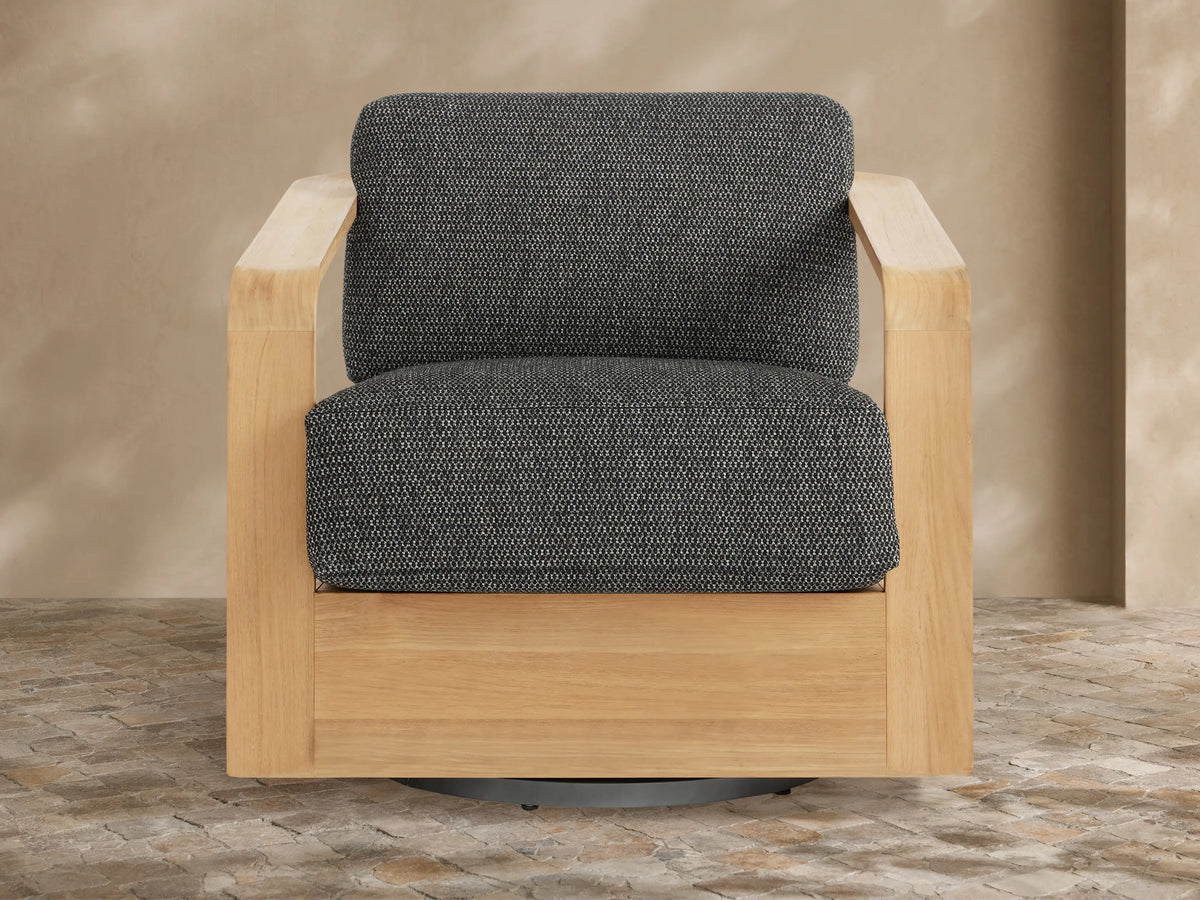 Sonoma Outdoor Teak Swivel Chair with natural golden teak frame and dark gray textured cushions, angled view on stone patio.