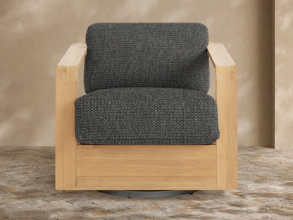 Sonoma Outdoor Teak Swivel Chair with natural golden teak frame and dark gray textured cushions, angled view on stone patio.