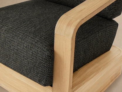 Sonoma Outdoor Teak Swivel Chair, front view. Light brown teak wood frame, dark grey cushions, on stone floor.