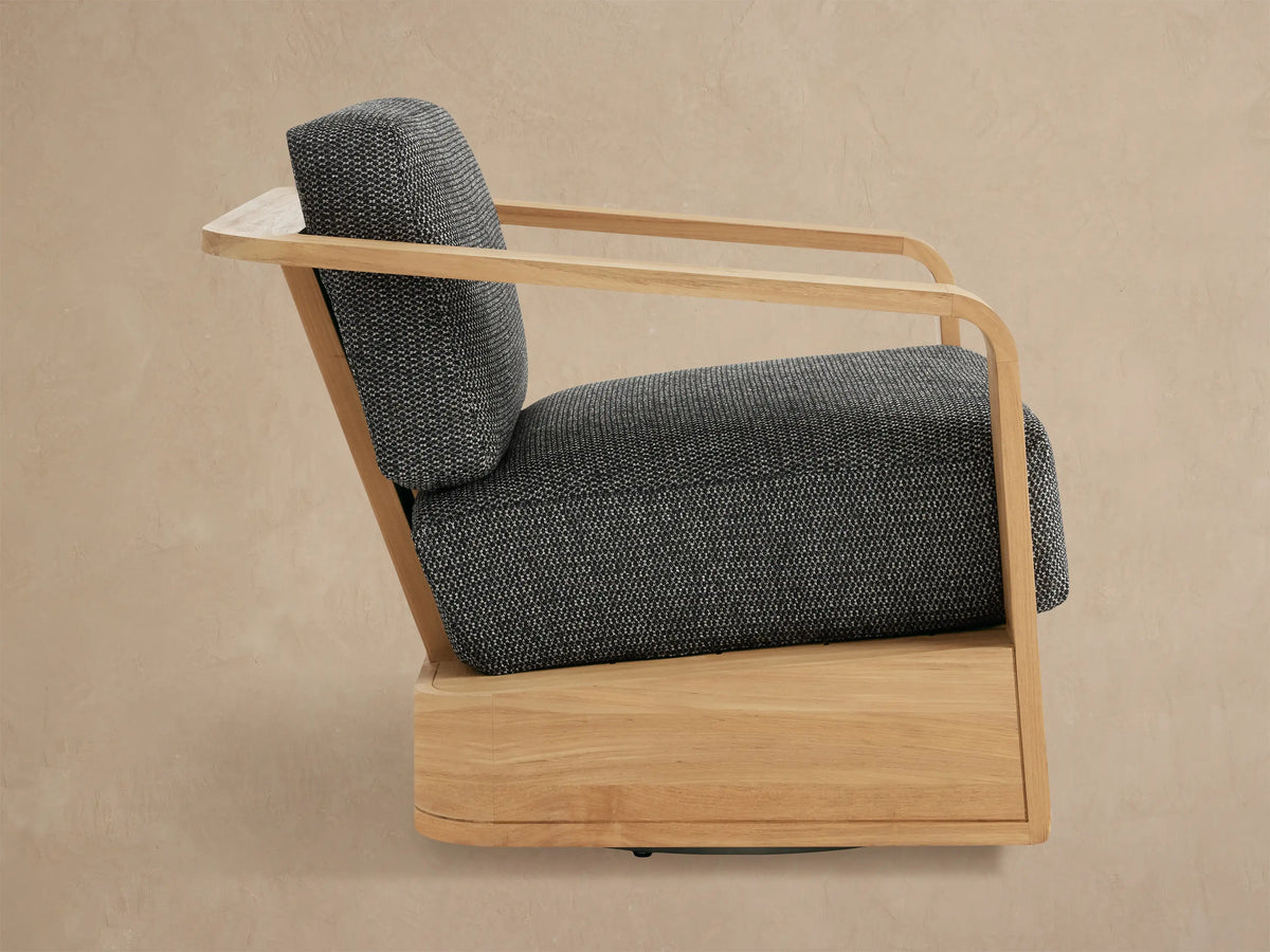 Close-up of Sonoma Outdoor Teak Swivel Chair. Light natural teak frame with curved armrest & dark gray textured cushions.