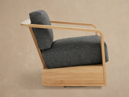 Close-up of Sonoma Outdoor Teak Swivel Chair. Light natural teak frame with curved armrest & dark gray textured cushions.