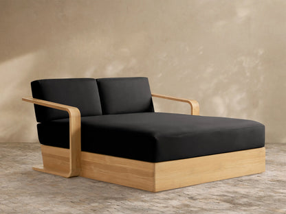 Sonoma Outdoor Teak Daybed with black cushions and light wood frame, angled on a patio against a neutral wall.