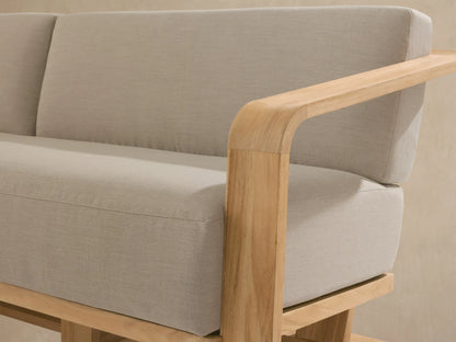 Sonoma Outdoor Teak Sofa: modern design with golden teak frame, curved arms, and light tan upholstered cushions on a stone patio.