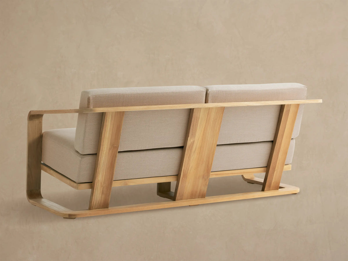 Sonoma Outdoor Teak Sofa. Close-up of light natural teak wood armrest with visible grain, light cream fabric seat and back cushions.