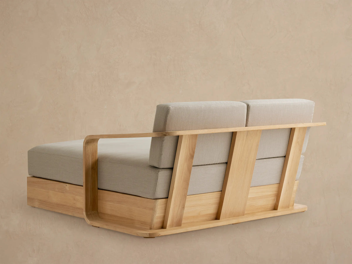 Close-up of Sonoma Outdoor Teak Daybed with a curved natural teak armrest and light greige seat and back cushions.
