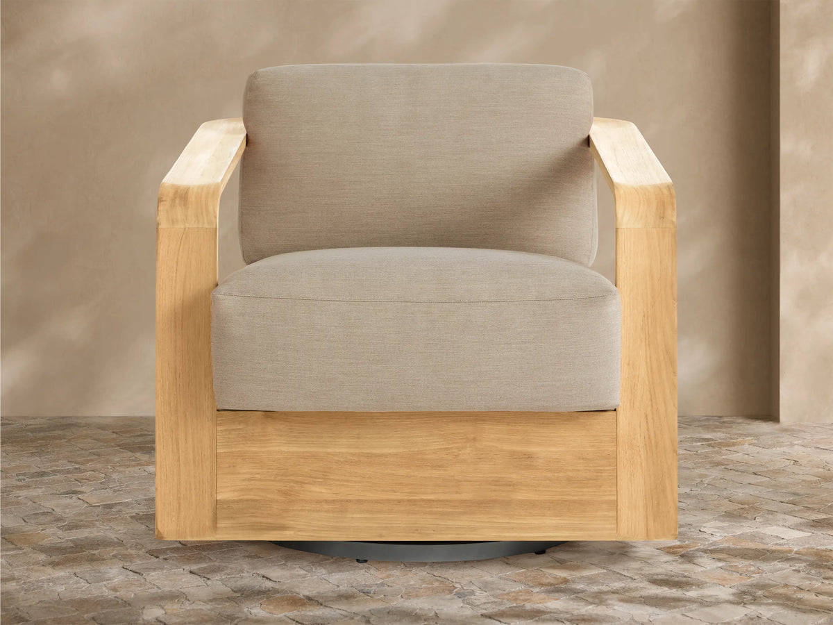 Sonoma Outdoor Teak Swivel Chair with light natural teak frame & light gray cushions, angled view on tiled patio.