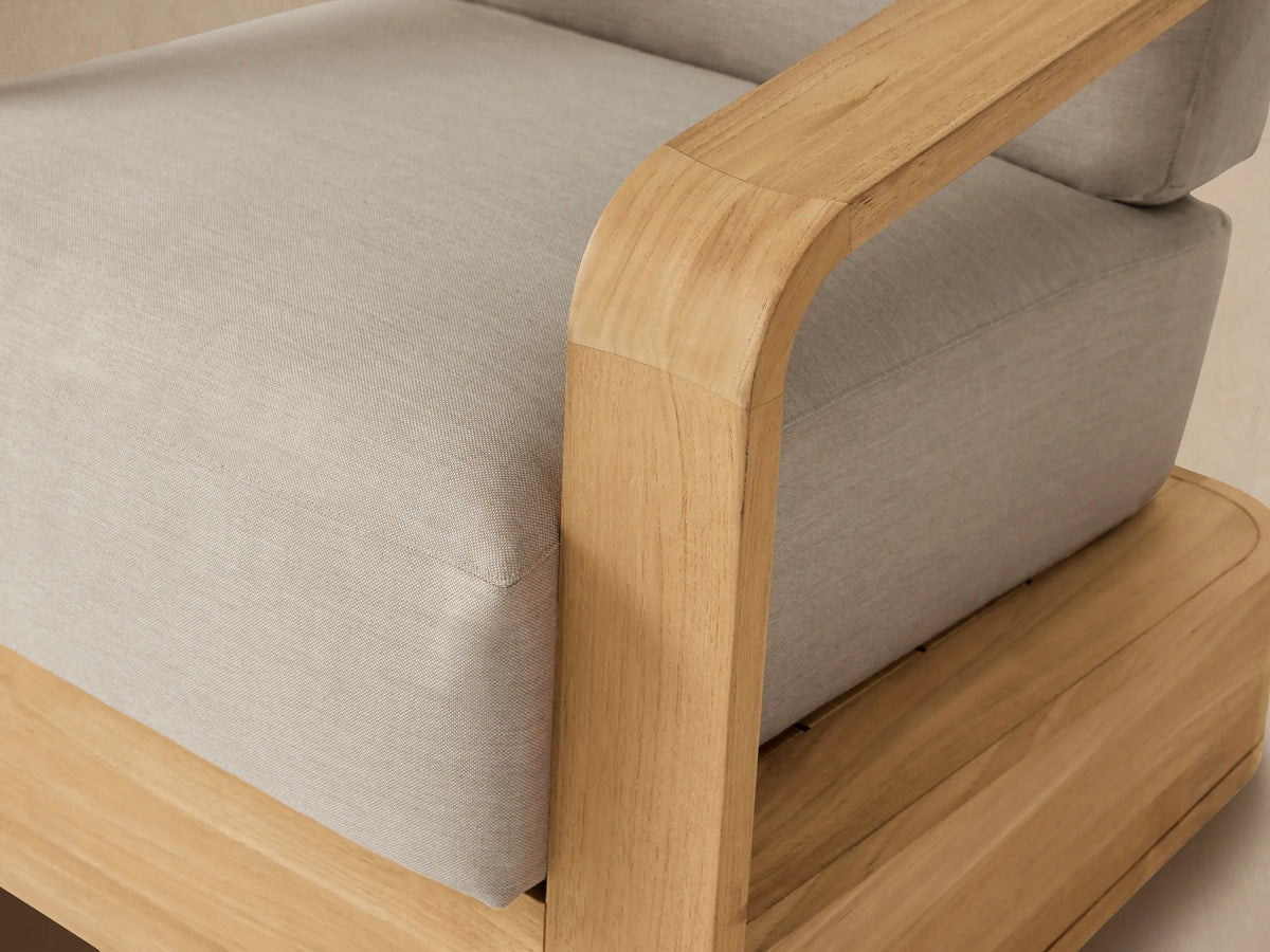 Sonoma Outdoor Teak Swivel Chair, natural light teak wood frame & armrests with thick light beige cushions, on patio.
