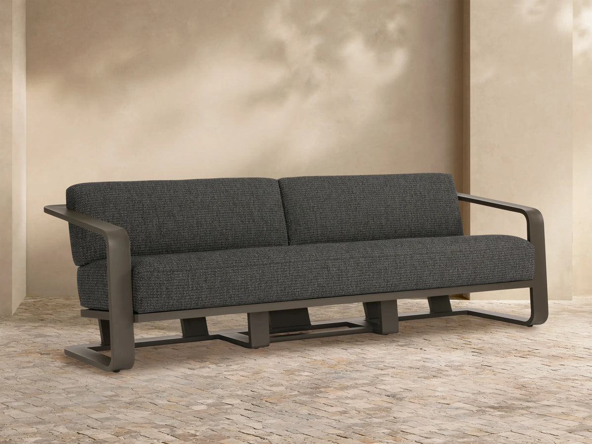 Sonoma Outdoor Aluminum Sofa, dark gray cushions on a sleek gray aluminum frame, on a tiled patio against a light wall.