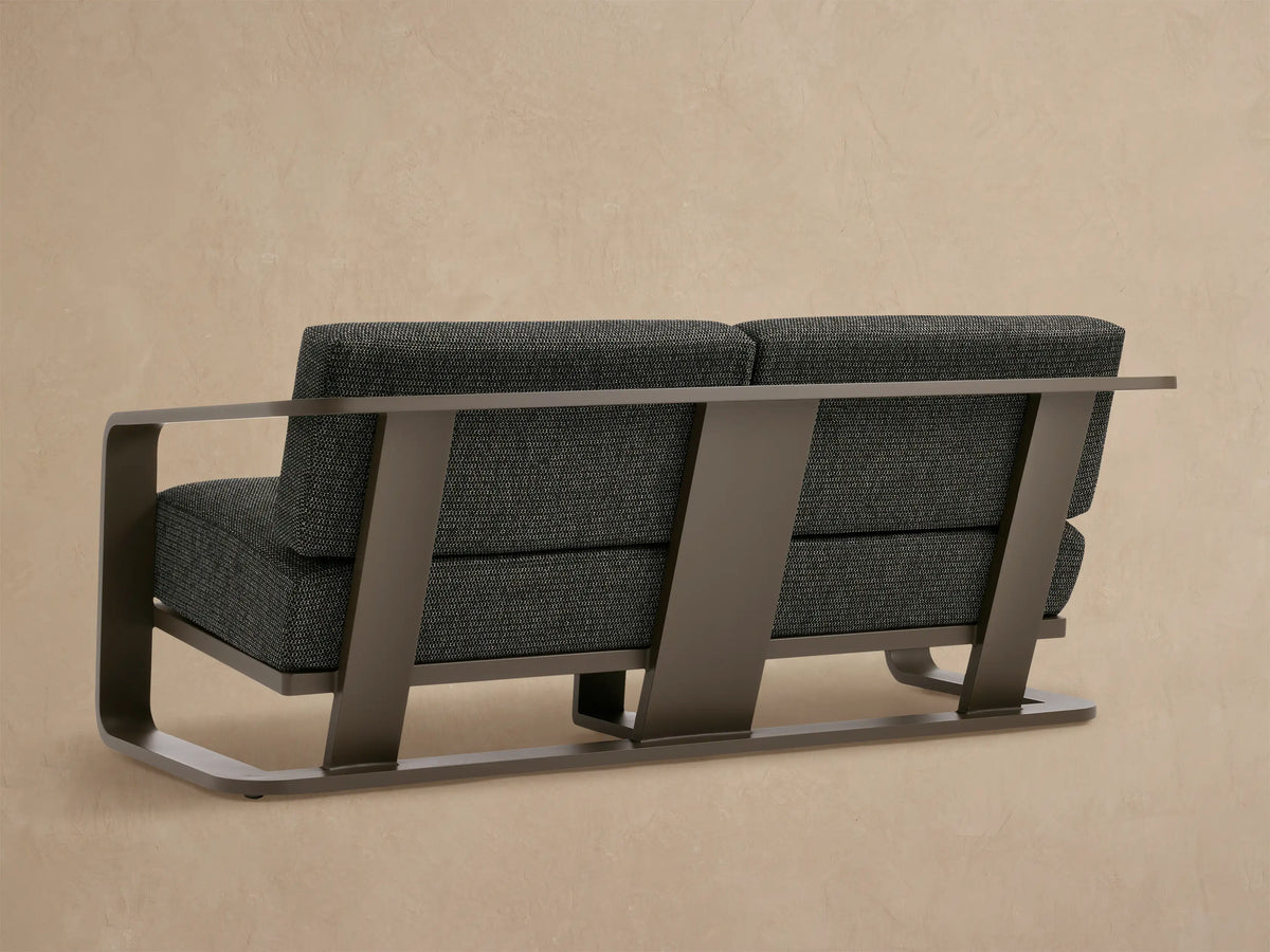 Close-up of Sonoma Outdoor Aluminum Sofa with dark gray speckled fabric cushions & curved bronze aluminum armrest.