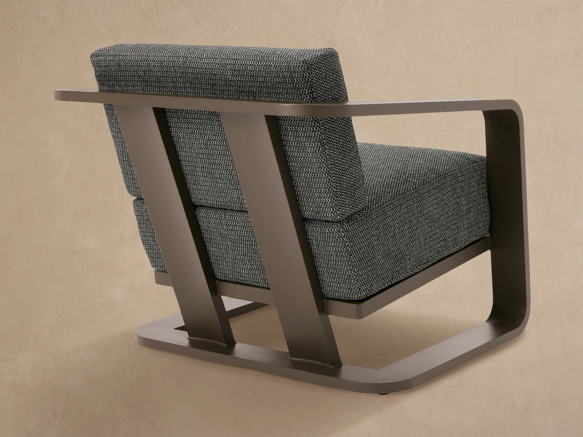 Close-up of Sonoma outdoor lounge chair's smooth brown aluminum armrest and textured dark grey fabric cushions.