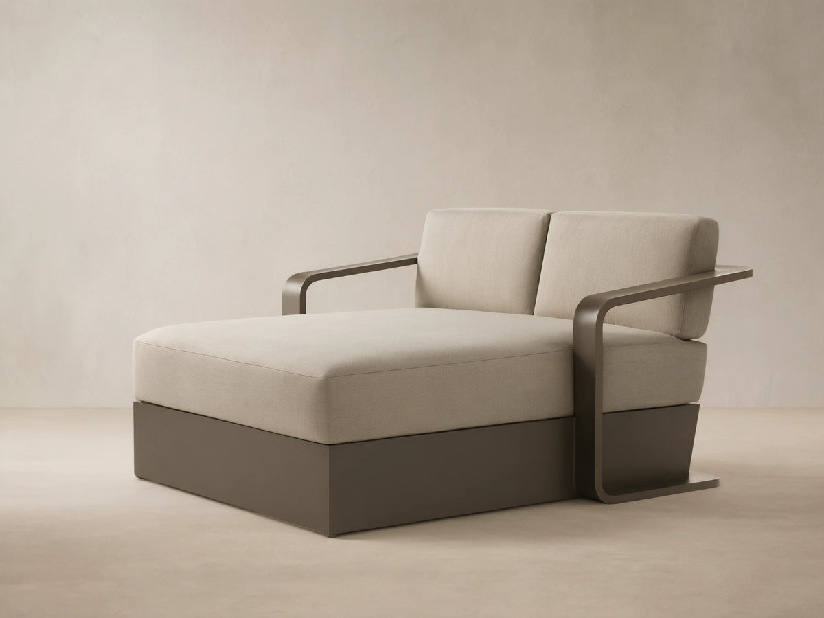 Angled Sonoma Outdoor Aluminum Daybed with light beige cushions and a dark bronze frame on a patio.