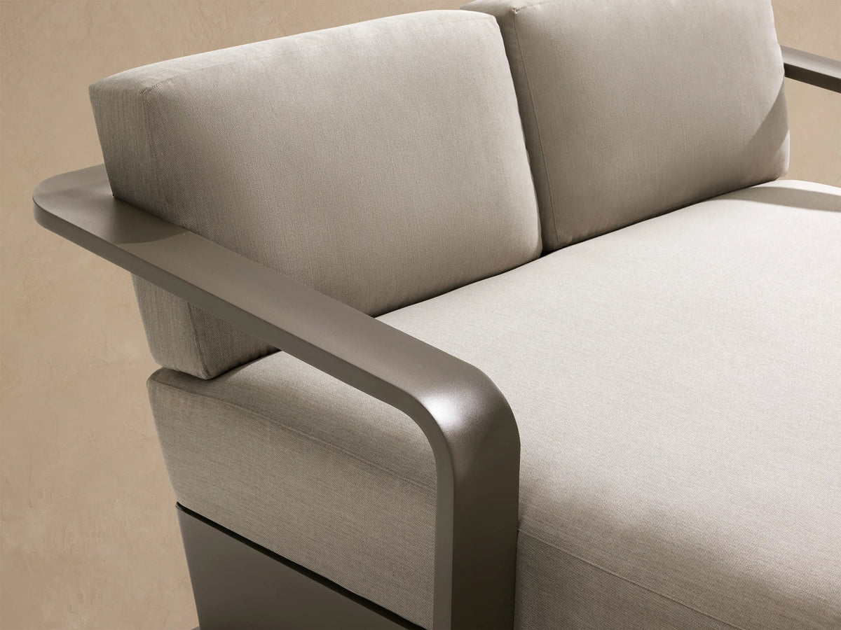 Sonoma Outdoor Aluminum Daybed, side view. Sleek dark gray aluminum frame with light beige cushions on a tan wall.