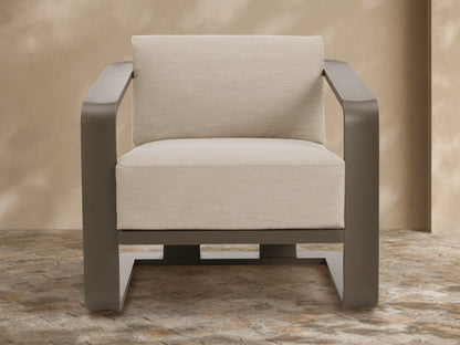 Sonoma Outdoor Aluminum Lounge Chair with dark bronze frame and light beige cushions, on a stone patio.