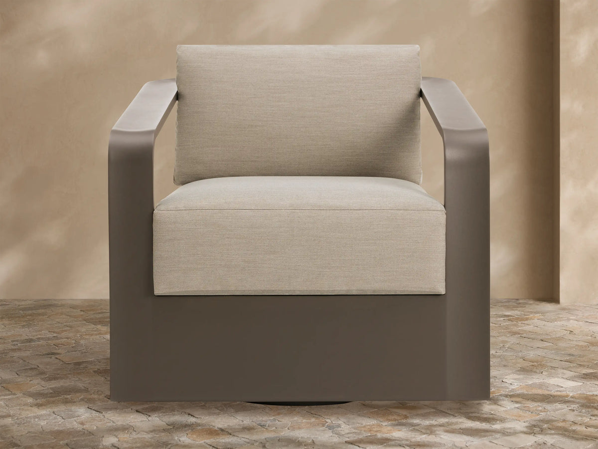 Sonoma Outdoor Aluminum Swivel Chair with sleek brown frame and thick, light beige cushions on a stone patio.