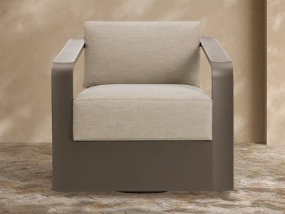 Sonoma Outdoor Aluminum Swivel Chair with sleek brown frame and thick, light beige cushions on a stone patio.