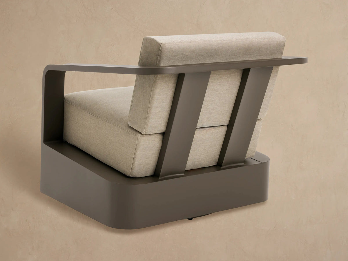 Close-up of Sonoma Outdoor Aluminum Swivel Chair. Dark bronze curved armrest, light taupe textured cushions, matching base.