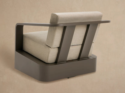 Close-up of Sonoma Outdoor Aluminum Swivel Chair. Dark bronze curved armrest, light taupe textured cushions, matching base.