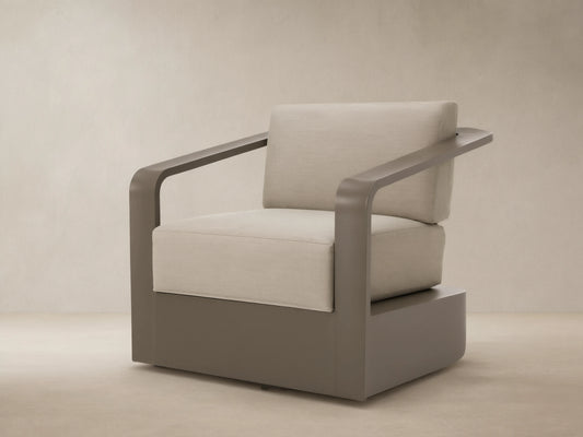 Sonoma Outdoor Aluminum Swivel Chair with sleek brown frame and thick, light beige cushions on a stone patio.